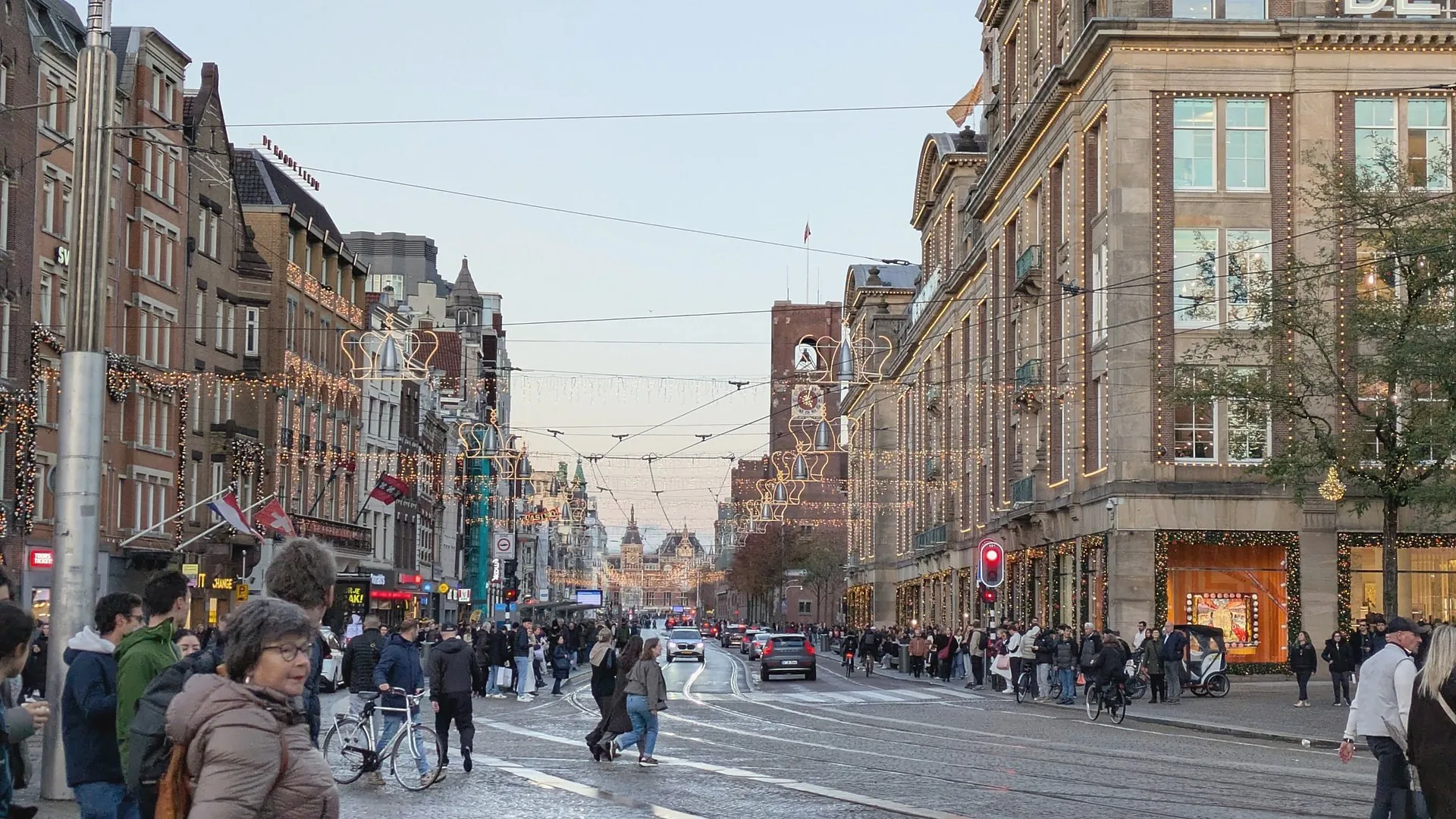 The Damrak at dusk with crown-shaped lights strung above the street, looking toward Centraal Station