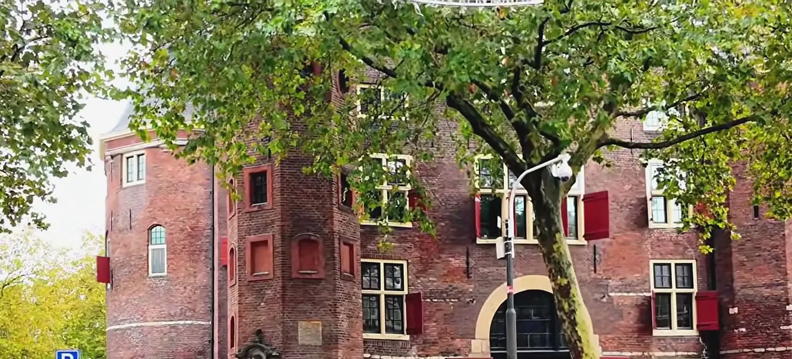 The red-brick towers and red shutters of De Waag, the 15th-century weigh house on Nieuwmarkt, behind autumn trees