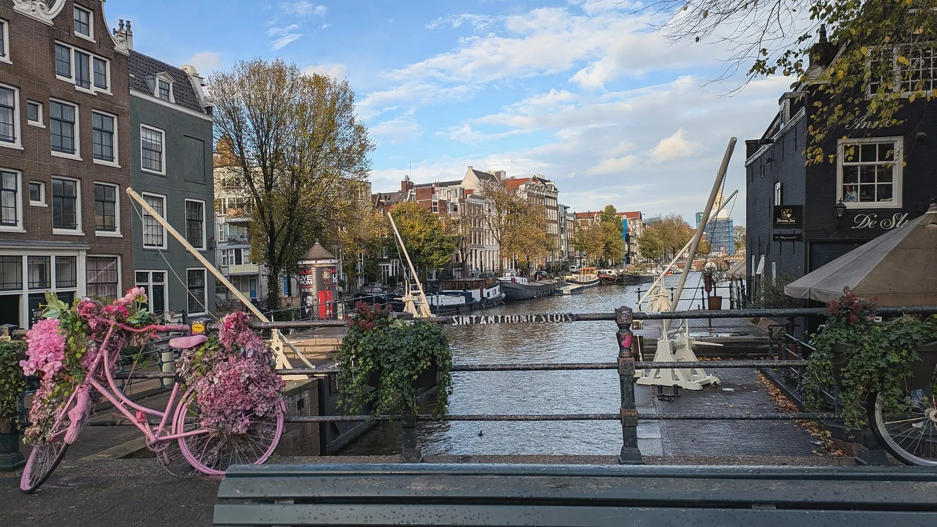 A pink bicycle covered in flowers leaning against a canal bridge railing in Amsterdam