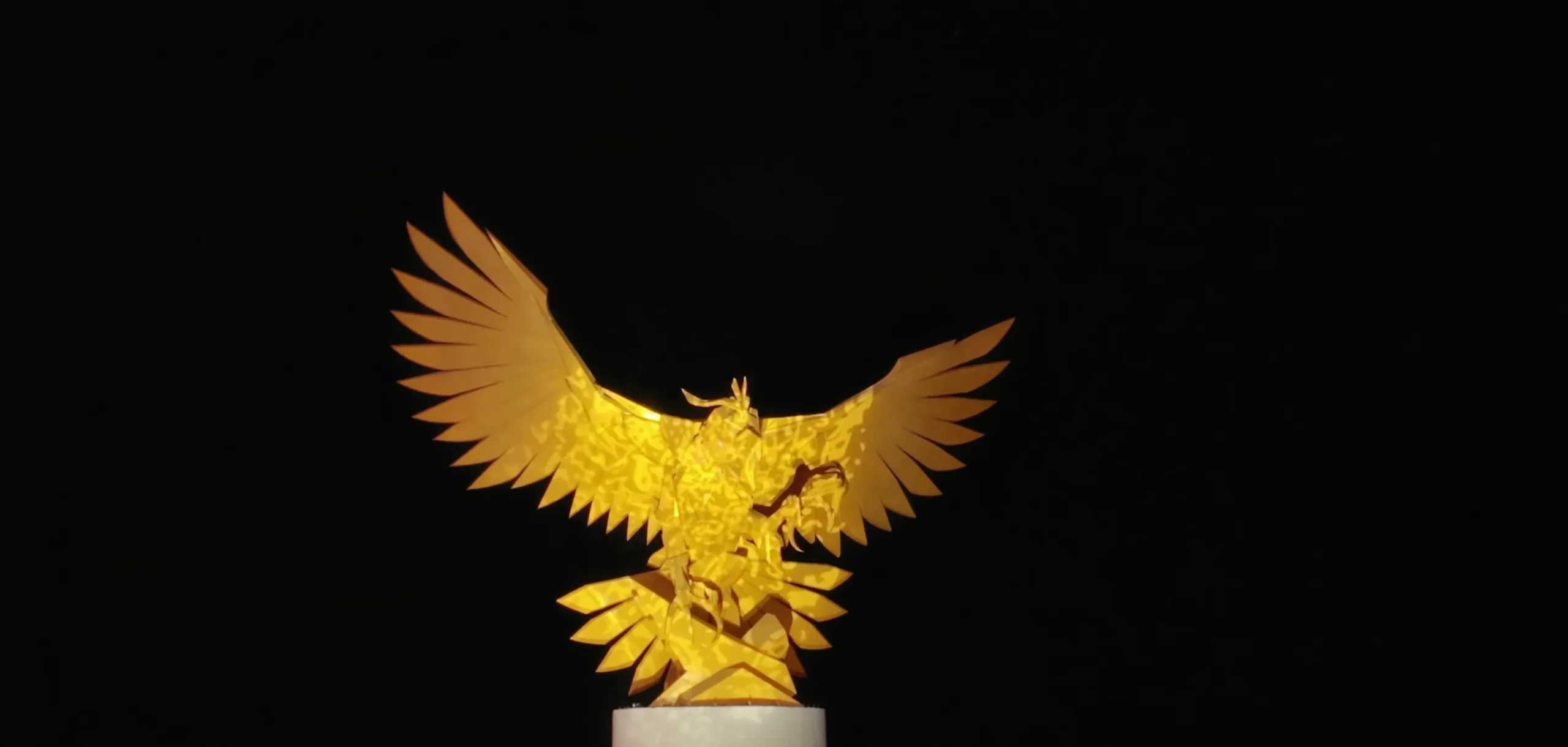 The Golden Falcon sculpture, wings spread on a white pedestal, lit against the night sky on the Jeddah Corniche