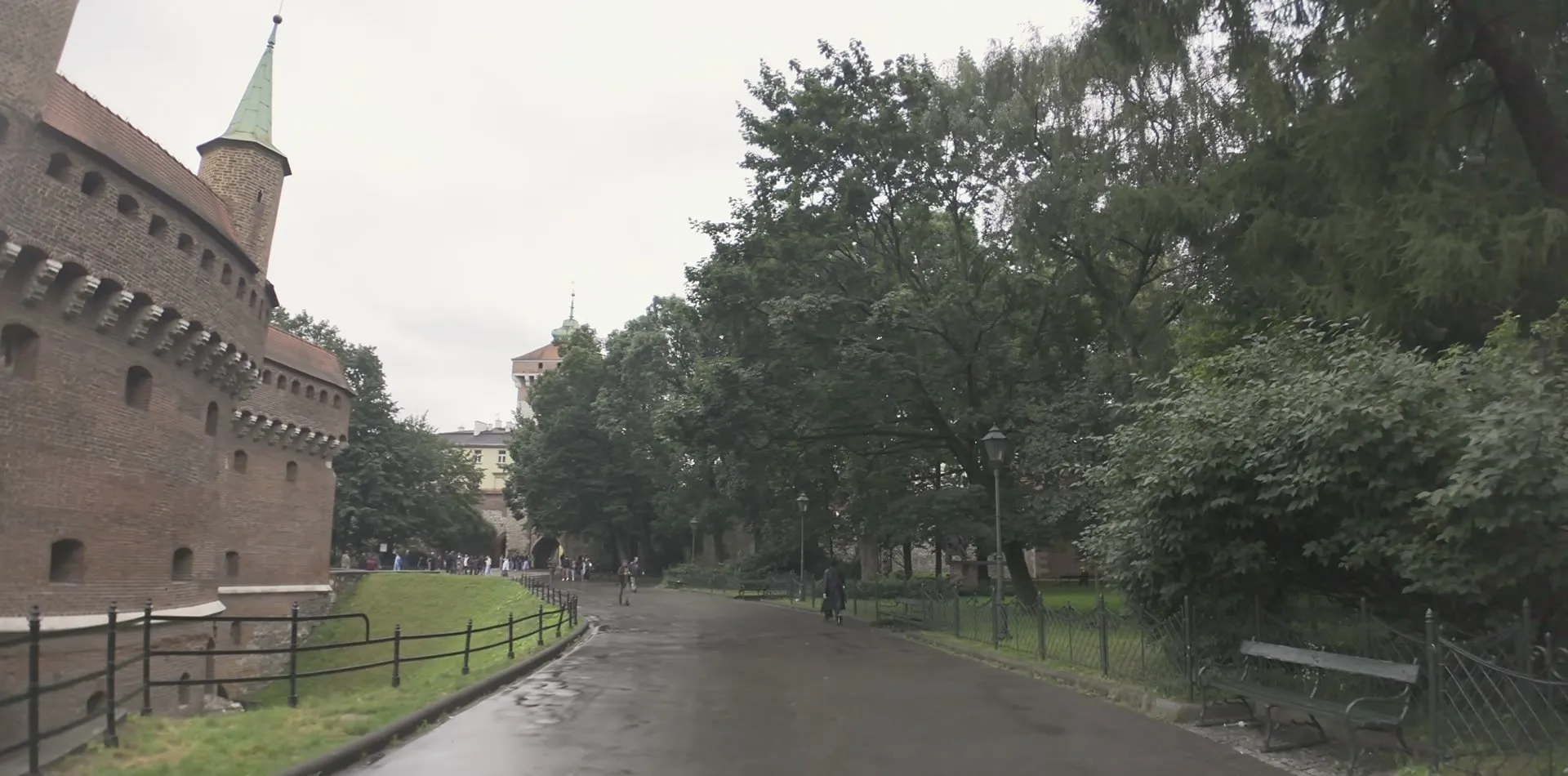 The round red-brick Barbican with its small turrets beside a wet path through the green Planty park in Kraków