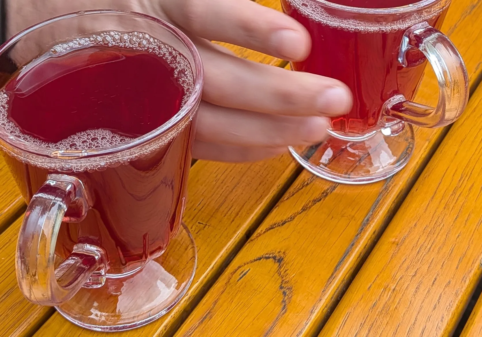 Two glass mugs of red kompot on a yellow wooden table