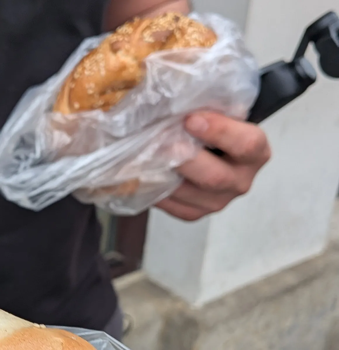 A hand holding an obwarzanek, Kraków’s ring-shaped bread, beside a small gimbal camera