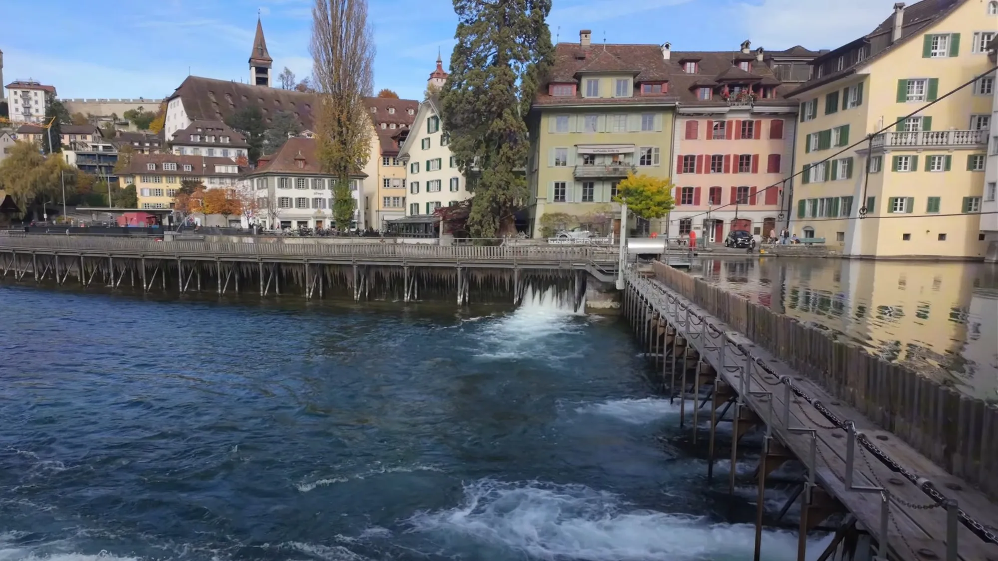 Water spilling white over the Nadelwehr weir on the Reuss in Lucerne, with old houses along the far bank