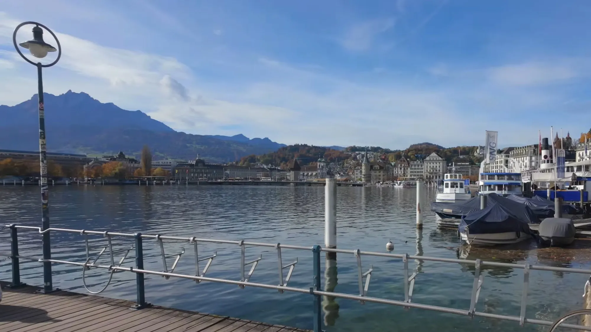 Lake Lucerne from a small pier off the Nationalquai on a sunny autumn day, with Pilatus on the left, the town across the water and moored boats on the right