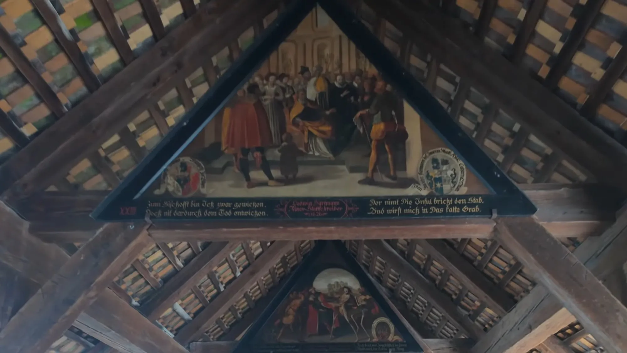 A triangular painting from the Dance of Death cycle under the wooden roof of the Spreuer Bridge in Lucerne, with verses lettered beneath it and a second painting further along the roof