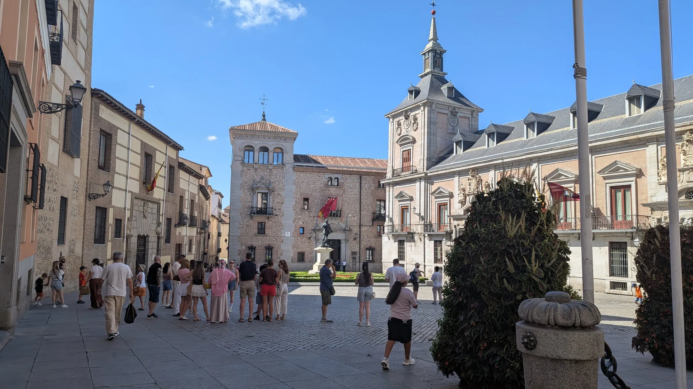 Plaza de la Villa in Madrid on a sunny day, with the brick Torre de los Lujanes, the slate spire of the Casa de la Villa, and a tour group gathered in the square