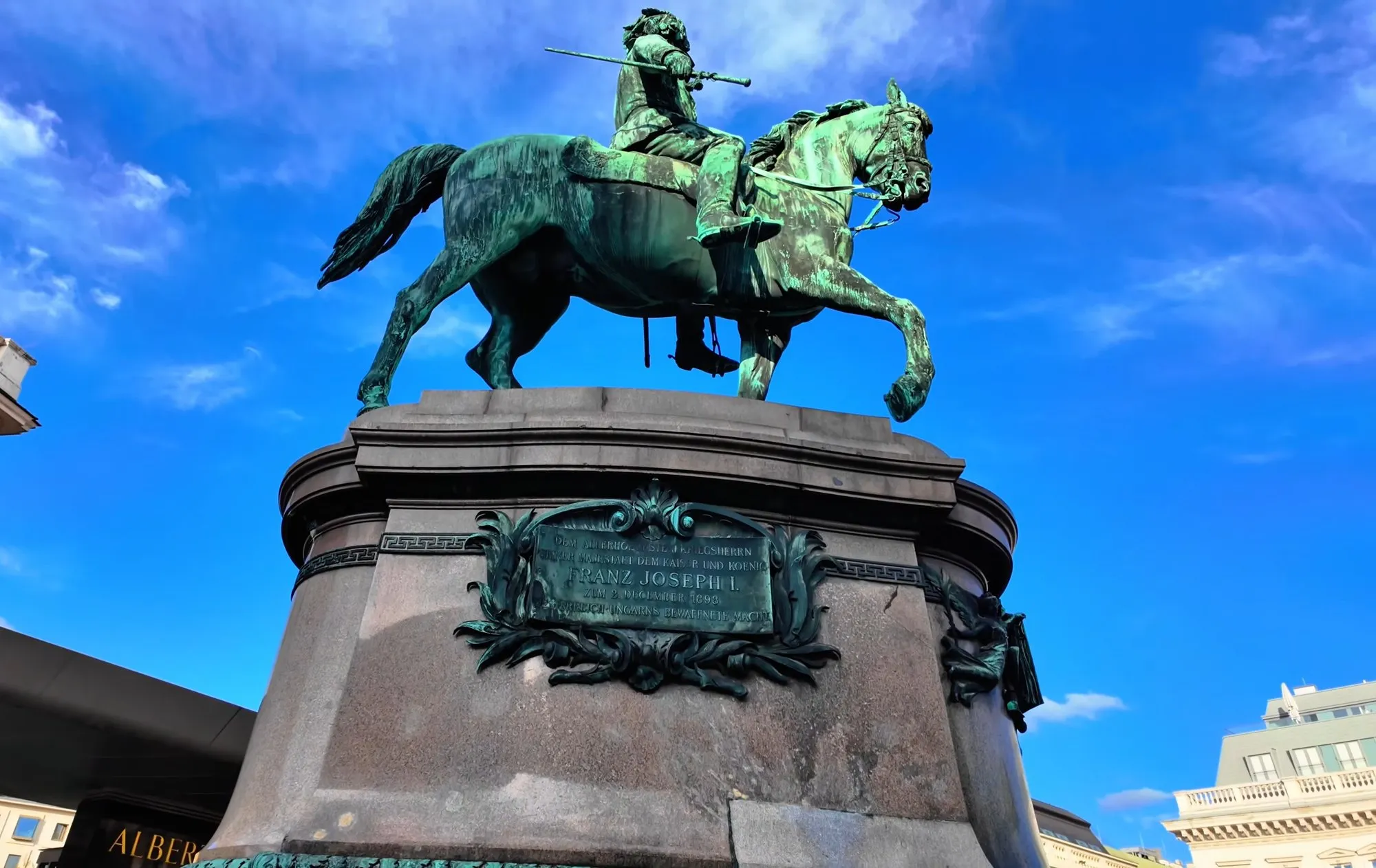 The bronze equestrian statue of Archduke Albrecht on its granite plinth on the Albertina terrace in Vienna, seen from below against a blue sky with clouds