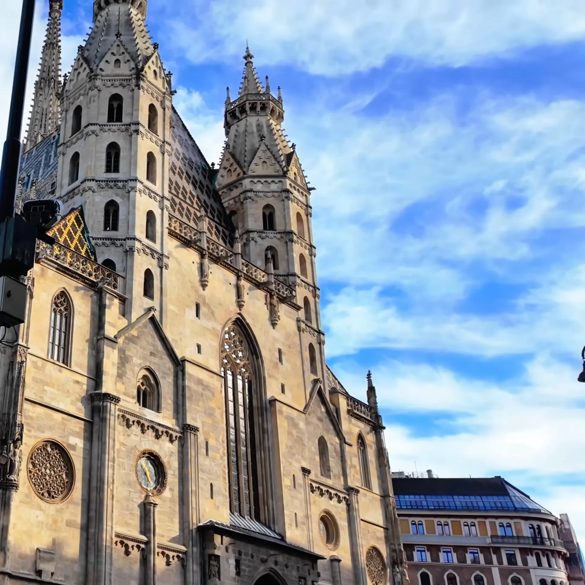 Stephansdom in Vienna seen from below on Stephansplatz, its pale stone towers, Gothic windows and patterned roof under a blue sky with white clouds